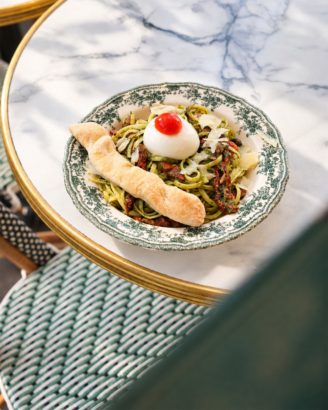 Assiette de pâtes au pesto, burrata et tomates servie dans la vaisselle verte de la trattoria
